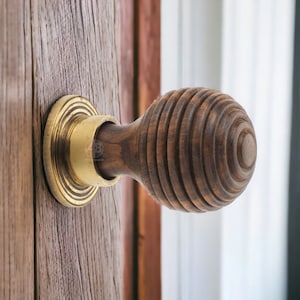 May include: A close-up shot of a wooden door knob with a spiral design. The knob is dark brown and attached to a wooden door. The base of the knob is gold. The door is made of wood with a natural grain, showing a rustic aesthetic.