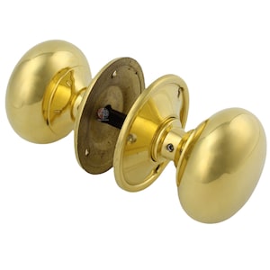 May include: A set of polished brass door knobs with an oval design. The door knobs are shown in pieces, with the mounting plates and connecting hardware visible. The hardware is a bright, shiny gold colour.