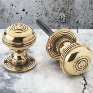 May include: Two polished brass door knobs. One is fully assembled, the other partially so, revealing the threaded rod. The knobs are round with concentric circle detailing. Ideal for interior doors.