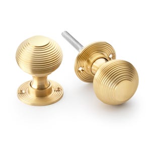 May include: Two brass door knobs with a grooved, spherical design. One is assembled, the other partially disassembled, showing the threaded rod. The knobs have a classic, elegant appearance.