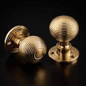 May include: Two polished brass door knobs featuring a spherical shape with horizontal ribbed detailing. Each knob is attached to a circular mounting plate with visible screw holes, showcasing a reflective metallic finish and a smooth, rounded design.