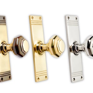 May include: Three door knobs with rectangular backplates. The knobs have an octagonal shape. The first knob is brass with a brown and tan knob. The second knob is brass with a gold knob. The third knob is silver with a silver knob.