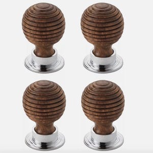 May include: Four wooden cabinet knobs with a grooved, spherical design. The knobs are a warm brown colour and sit atop a shiny, silver-coloured base. The knobs are arranged in a square formation against a light background.