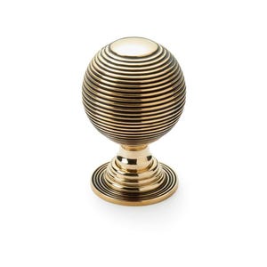May include: A gold-coloured, spherical cabinet knob with a grooved design. The knob sits on a matching base with concentric circles. The hardware is likely made of metal and is set against a white background.