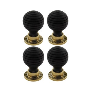 May include: Four black, spherical cabinet knobs with a grooved texture. Each knob sits atop a brass-coloured base with concentric circular detailing. The knobs are arranged in a square formation against a white background.