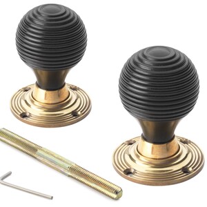 May include: Two black and brass door knobs with a ribbed design. The knobs have a round shape and are mounted on brass circular bases. A threaded rod and an Allen key are also included.