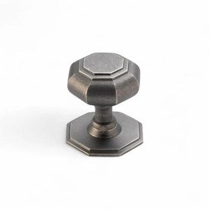 May include: An antique-style cabinet knob with an octagonal design. The knob is made of a dark, metallic material with a weathered finish. The base and the knob itself have a multi-faceted shape, adding to its vintage appeal. Suitable for furniture.
