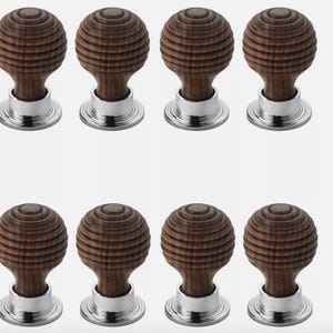 May include: Eight wooden cabinet knobs with a grooved, spherical design. The knobs are a dark brown colour and sit on a shiny, silver-coloured base. The knobs are arranged in two rows of four.