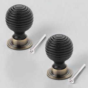 May include: Two black cabinet knobs with a grooved, spherical design. Each knob has a bronze-coloured base and comes with a silver screw for installation. Suitable for drawers and cabinets.