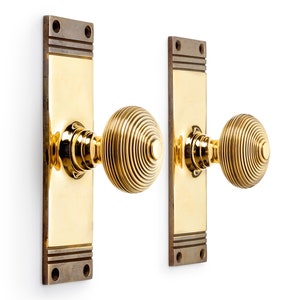 May include: A pair of brass door knobs and backplates. The knobs have a spiral design, and the rectangular backplates have a contrasting finish at the top and bottom. The door hardware is shown against a white background.