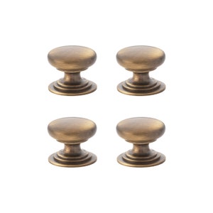 May include: Four antique brass cabinet knobs with an oval top and a decorative base. The knobs are arranged in a square formation against a white background. Each knob is approximately 3.2 cm in diameter.