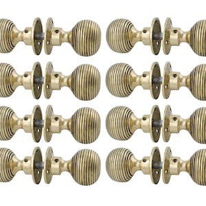 May include: Twelve brass door knobs, each featuring a ribbed, spherical design and a circular backplate. The hardware has a warm, golden hue, indicative of an antique or vintage style. The knobs are presented against a white backdrop, highlighting their details.