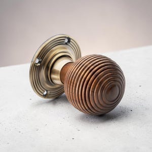 May include: A wooden door knob with a grooved sphere design and a brass-toned circular base. The knob is a warm brown colour, and the base has an antique finish. Suitable for interior doors, the knob's diameter is approximately 6 cm.