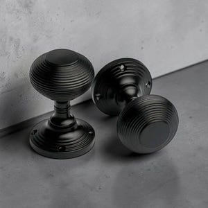 May include: Three black door knobs with a ribbed, spherical design. The knobs have a classic, elegant look, with a round base and a matching backplate. The hardware is made of metal and has a matte finish.