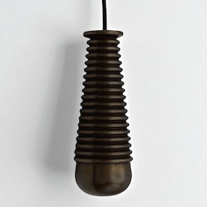 May include: A dark brown, ribbed light pull with a rounded base and a cylindrical top. It hangs from a black cord against a white backdrop. The design is simple and elegant, suitable for various interiors.