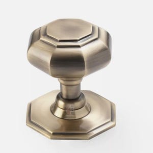 May include: An antique brass door knob with an octagonal design. The knob has a detailed, geometric shape and a warm, metallic finish. This hardware piece is suitable for interior doors and adds a touch of vintage charm.