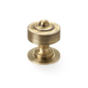 May include: A brass-coloured cabinet knob with a round, ribbed design. The knob has a small, rounded top and a base with concentric circles. The hardware is designed for furniture and home decor.
