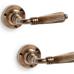 May include: Two antique bronze door handles. Each handle features a circular base with screw holes and a ribbed, cylindrical grip. The handles are set against a white background, highlighting their aged, metallic finish.