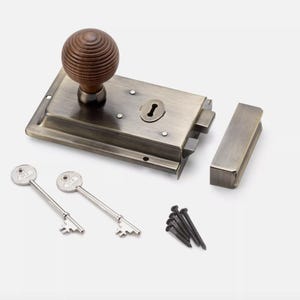 May include: Antique brass door latch set with a wooden knob, two keys, and mounting hardware. The latch features a rectangular backplate, a keyhole, and a matching strike plate. The wooden knob is round with a grooved design.