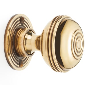 May include: A polished brass door knob with a round, ridged design. The knob features concentric circles and a circular backplate. The hardware is designed for a door and is made of brass.