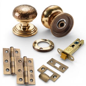 May include: A selection of antique brass door hardware, including two doorknobs, hinges, a latch, and a strike plate. One doorknob has a hammered texture. The hardware is displayed on a white background.