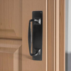May include: A black door pull handle fixed to a light-coloured wooden door. The handle features a rectangular backplate and a curved handle. The door is constructed from vertical wooden planks.