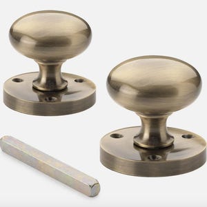 May include: Two antique brass door knobs with an oval shape and a matching spindle. The knobs have a classic design with a round base and a smooth, polished finish. The hardware is suitable for interior doors.