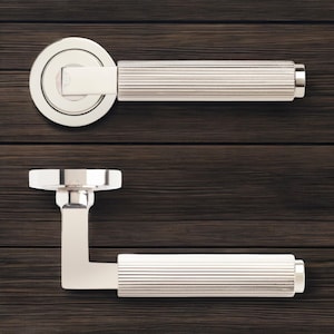 May include: Two polished silver door handles. One has a circular backplate and a straight, ridged handle. The other is L-shaped with a ridged handle. Both are set against a dark wood grain background.