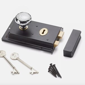 May include: A black door latch with a decorative, faceted knob. The latch includes a strike plate, two keys, and mounting screws. The keyhole is surrounded by a brass-coloured plate.