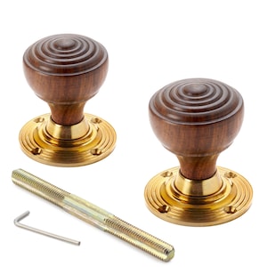 May include: Two wooden door knobs with brass bases, a threaded rod, and a hex key. The dark brown knobs have concentric circles. The circular brass bases have a ridged design. The door knobs are for interior doors.