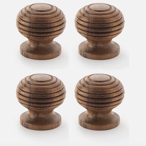 May include: Four wooden cabinet knobs with a spherical design. Each knob is a warm brown colour and features a series of concentric rings, creating a textured, layered effect. The knobs have a classic, timeless aesthetic.