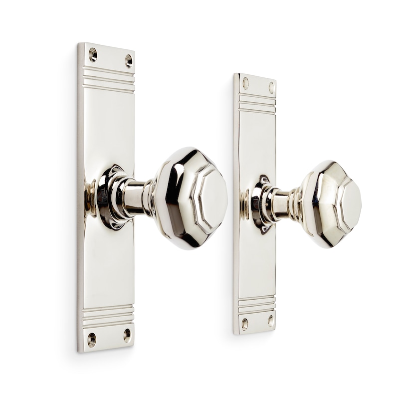 May include: Polished nickel door hardware set. The set includes two rectangular backplates with horizontal grooves and two faceted doorknobs. The hardware is designed for a door and is mounted on a white background.