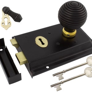 May include: A black door latch with a grooved, spherical knob and two keys. The latch features brass-coloured accents and a matching strike plate. The set includes a separate handle and a black metal strike plate.