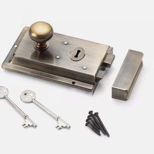 May include: Antique brass door latch set with two keys and screws. The rectangular latch has a round knob and keyhole. The set includes a strike plate and screws for installation. A classic door hardware set.