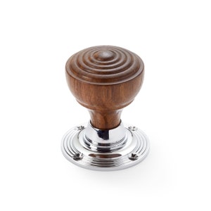 May include: A wooden door knob with a polished, dark brown, circular top and a chrome base. The knob has a classic design with concentric circles carved into the wood. The base is round with a series of concentric grooves.