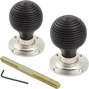 May include: Two black door knobs with a grooved, spherical design, mounted on silver-coloured circular bases. A long, threaded rod and an Allen key are also included, suggesting a hardware or home improvement product.