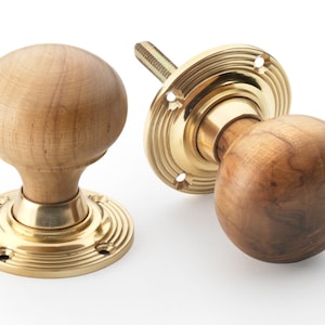 May include: Two wooden door knobs with brass bases. The spherical knobs are made of light brown wood, displaying the grain. The brass bases have a circular design with screw holes. One knob is disassembled, showing the screw.