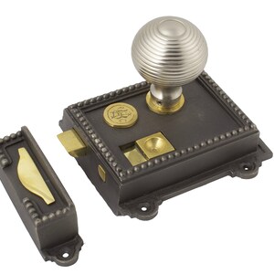 May include: A detailed image of a vintage door latch set. The set includes a dark grey rectangular base with a decorative border, a round, ridged silver knob, and a separate latch piece. Brass-coloured accents are visible.