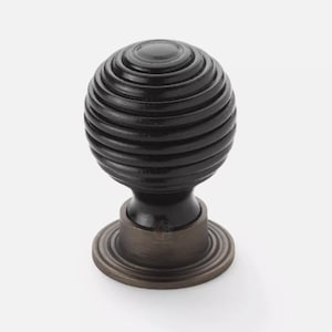 May include: A dark brown, spherical cabinet knob with a grooved design. The knob sits on a dark bronze base with a circular, ridged design. This decorative hardware is suitable for drawers and cabinets.