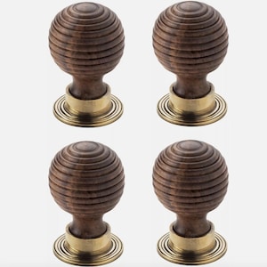 May include: Four wooden door knobs with a spherical design. The knobs are a dark brown colour with a grooved texture. They have a brass-coloured base and are set against a white background. Suitable for furniture or doors.