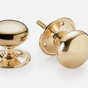 May include: Two polished brass door knobs. One assembled, one disassembled showing the mounting plate and threaded post. The knobs have a rounded, smooth design and a shiny finish. Ideal for interior doors.