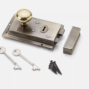 May include: Antique brass door latch set with a hammered knob, two keys, and mounting hardware. The rectangular latch features a keyhole and a separate strike plate. Ideal for vintage or rustic decor.