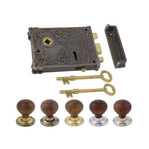 May include: An antique-style door lock set featuring a dark grey metal lock with decorative scrollwork, two brass keys, and a selection of wooden door knobs with brass and silver-toned bases. The lock has a keyhole.