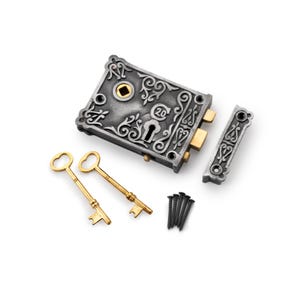 May include: An antique-style lock set with a silver finish, ornate scrollwork, and gold-coloured accents. The set includes a rectangular lock, a separate latch, two gold keys, and a small pile of black screws. The lock has the number "20" engraved on it.