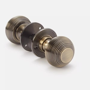 May include: Antique brass door knob set with a round, grooved design. The set includes two knobs, a connecting rod, and a mounting plate. The knobs have a warm, metallic finish and a classic, vintage aesthetic.