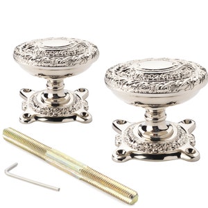 May include: Two decorative silver door knobs with intricate floral designs. The knobs feature a rounded top and a detailed base. A long screw and an Allen key are also included.