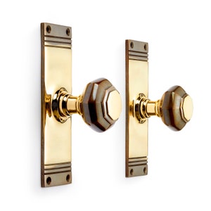 May include: A pair of brass door handles with a rectangular backplate and a decorative, faceted knob. The knobs have a brown and gold color scheme, and the backplates have a two-tone design.