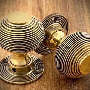 May include: Three antique brass door knobs with a spherical design and concentric grooves. The knobs are mounted on circular bases. The brass has a warm, aged patina, suggesting vintage hardware. The knobs are suitable for doors.