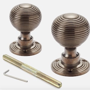 May include: Two antique bronze door knobs with a ribbed, spherical design. The knobs sit on a circular base and are accompanied by a long screw and an Allen key. The hardware has a vintage aesthetic.
