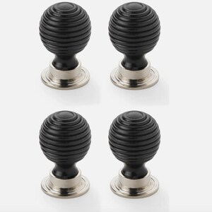 May include: Four black cabinet knobs with a ribbed, spherical design. Each knob has a silver-coloured base. The knobs are arranged in a square formation against a white background, suitable for furniture or home decor.